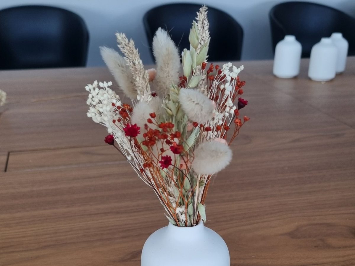 Petit bouquet de fleurs séchées composé en atelier Maison Punch — épis de blé, lagurus, gypsophile et fleurs rouges — dans un vase blanc posé sur une table en bois
