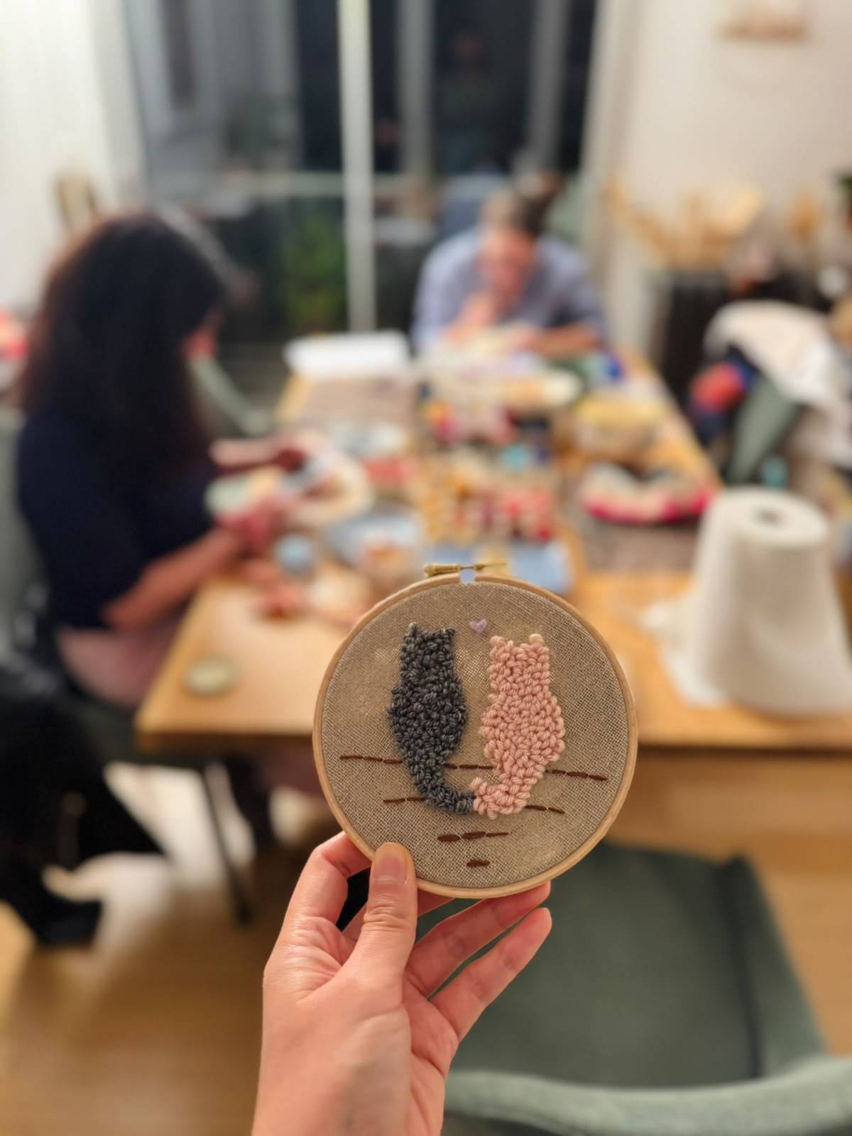 Deux chats brodés au punch needle sur un tambour en bois, tenus en main pendant un atelier à Paris