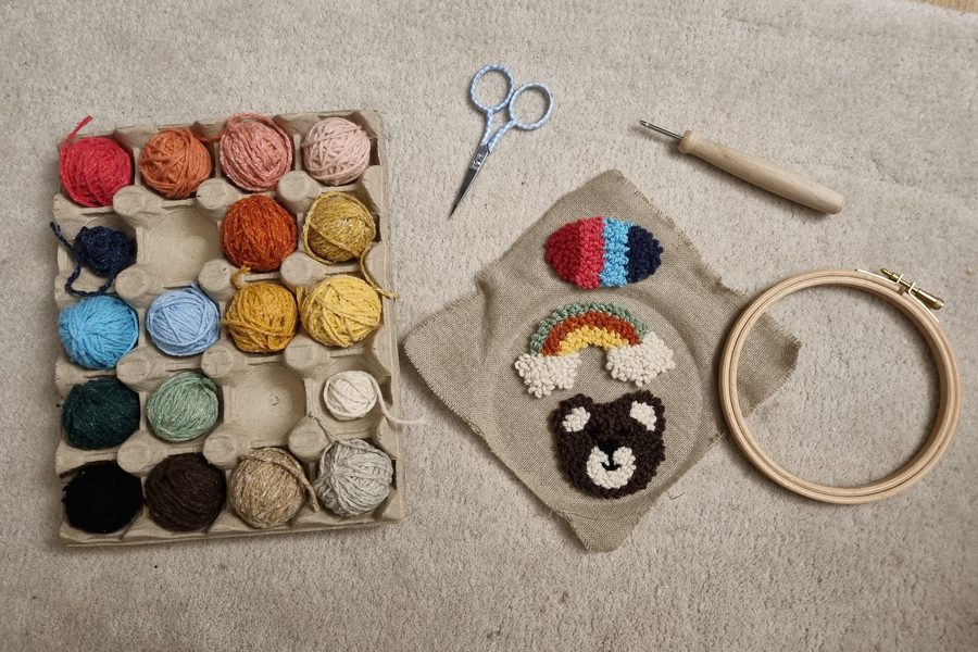 Matériel d'un atelier de punch needle : tambour à broder, poinçon, ciseaux, toile brodée en relief et pelotes de laine colorées