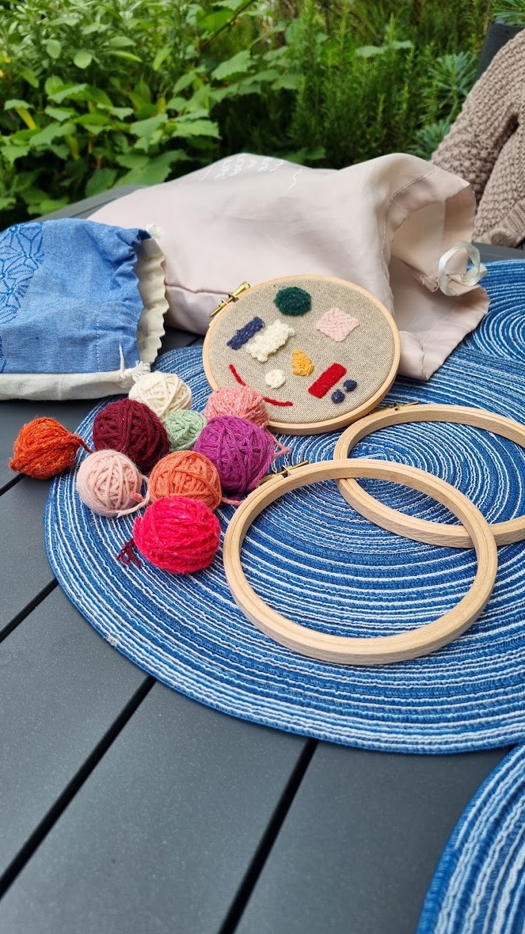 Matériel de punch needle posé sur une table : tambours en bois vides, pelotes de laine colorées et toile tendue portant des échantillons de points