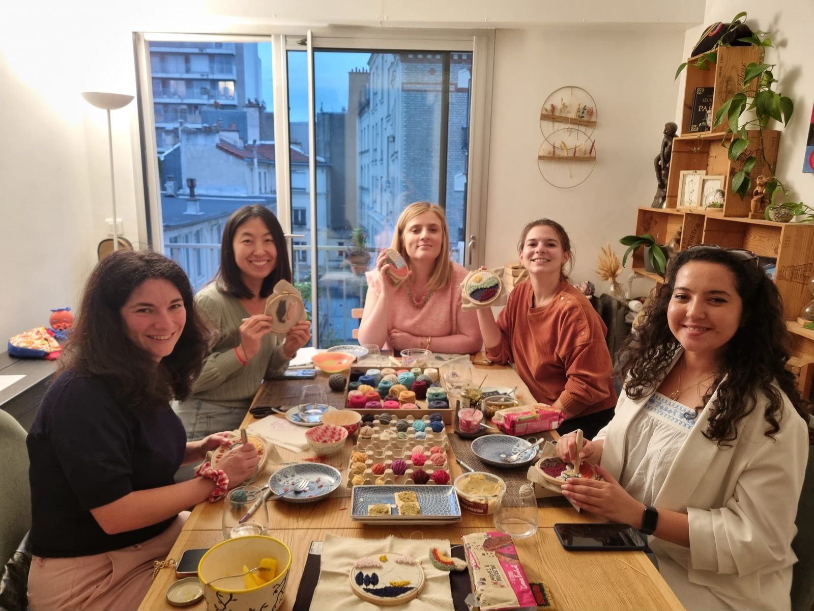 Cinq participantes d'un atelier Maison Punch autour de la grande table, leurs pièces en punch needle terminées à la main