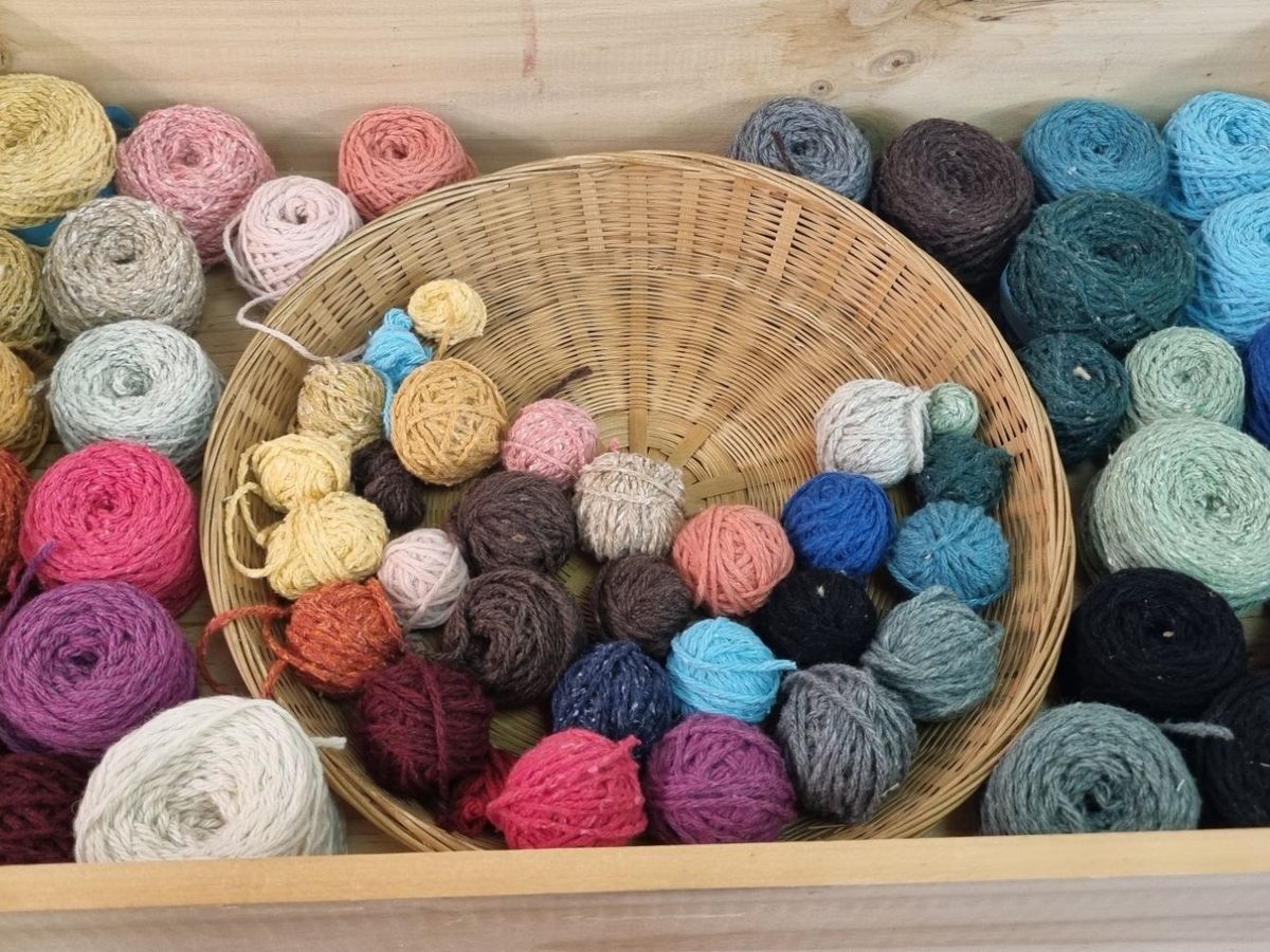 Une caisse en bois remplie de pelotes de laine de toutes les couleurs, avec au centre une corbeille en osier pleine de petites pelotes
