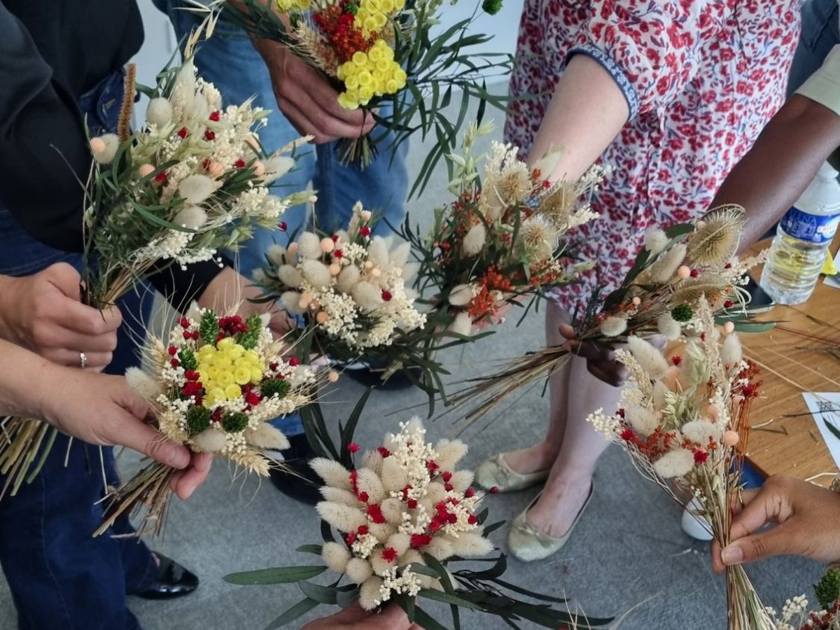 Fin d'un atelier fleurs séchées : huit participants tendent vers le centre le petit bouquet qu'ils viennent de composer